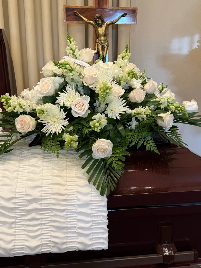 A white and green casket spray of roses, hydrangea and anthurium.