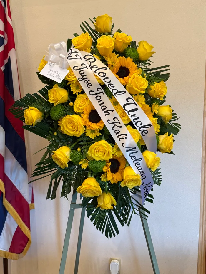 A yellow and orange standing spray on a floor easel with a hand lettered ribbon sash.
