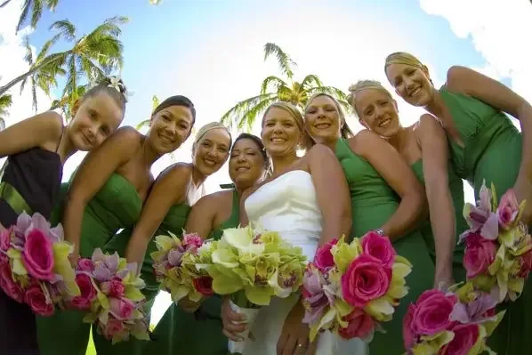 A bridal party in green dresses holding bouquets, photographed from below against palm trees.