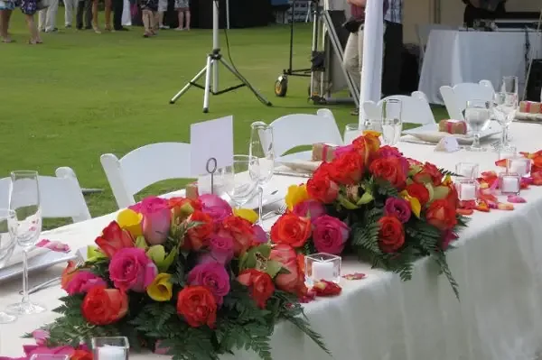 A long reception table lined with bright rose and orchid centerpieces, set before guests arrive.