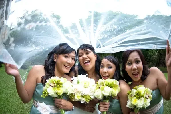 Bridesmaids under a lifted veil holding white and green bouquets.