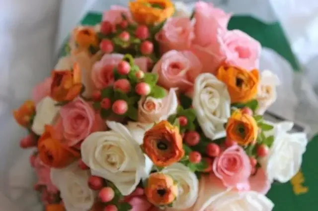 A close view of a bouquet of peach, pink and cream roses with red berries.
